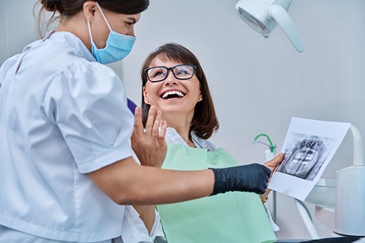 Woman smiling with dentist while reviewing X-ray