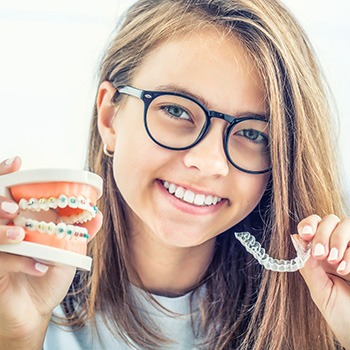 Girl holding sample braces in one hand and clear aligner in the other
