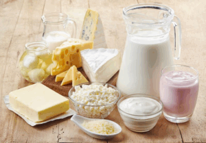 A pitcher of milk and several other dairy products arranged on a wood surface